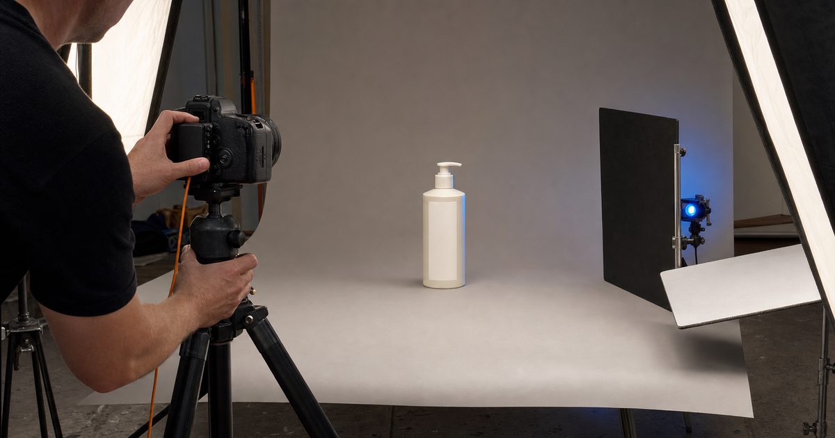 Photographer framing a plain white pump bottle on a neutral studio sweep between two softboxes